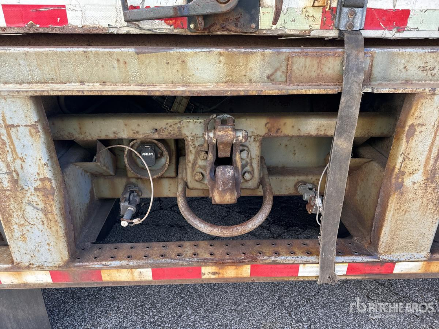 Trailer hitch area showing coupling with ground connection and rusted components; visible toolbox and frame under rear of van trailer.