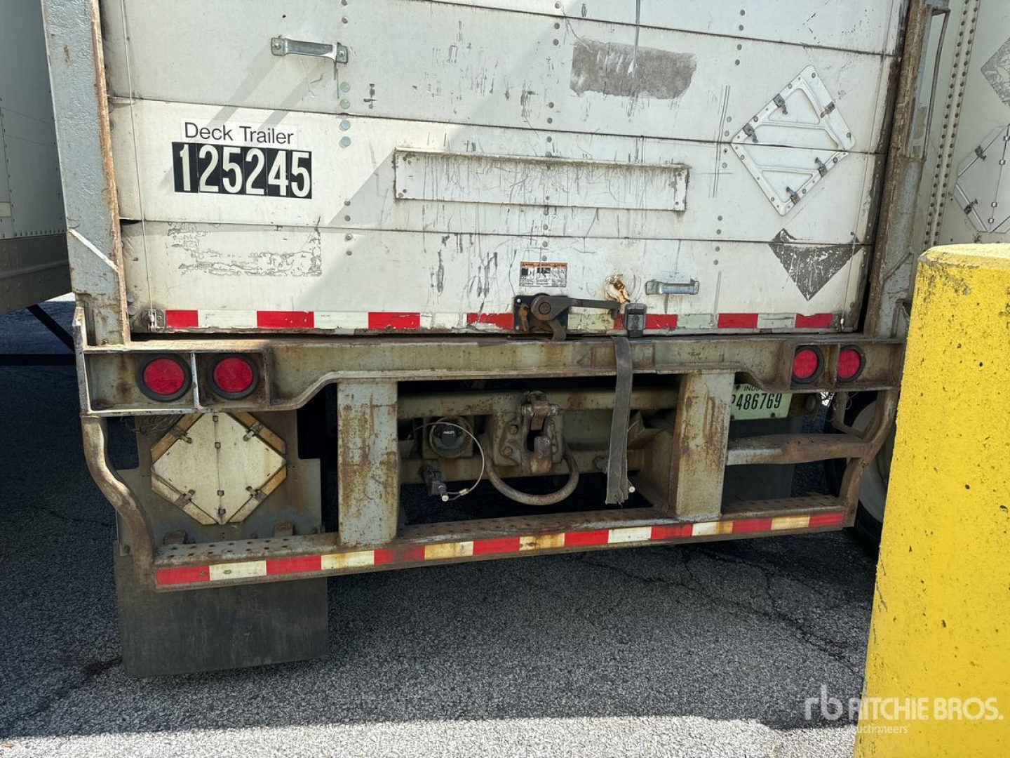 Back of a white Wabash trailer with deck trailer plate 125245, various reflective strips, taillights, and a hitch assembly in the center; some dirt and wear.