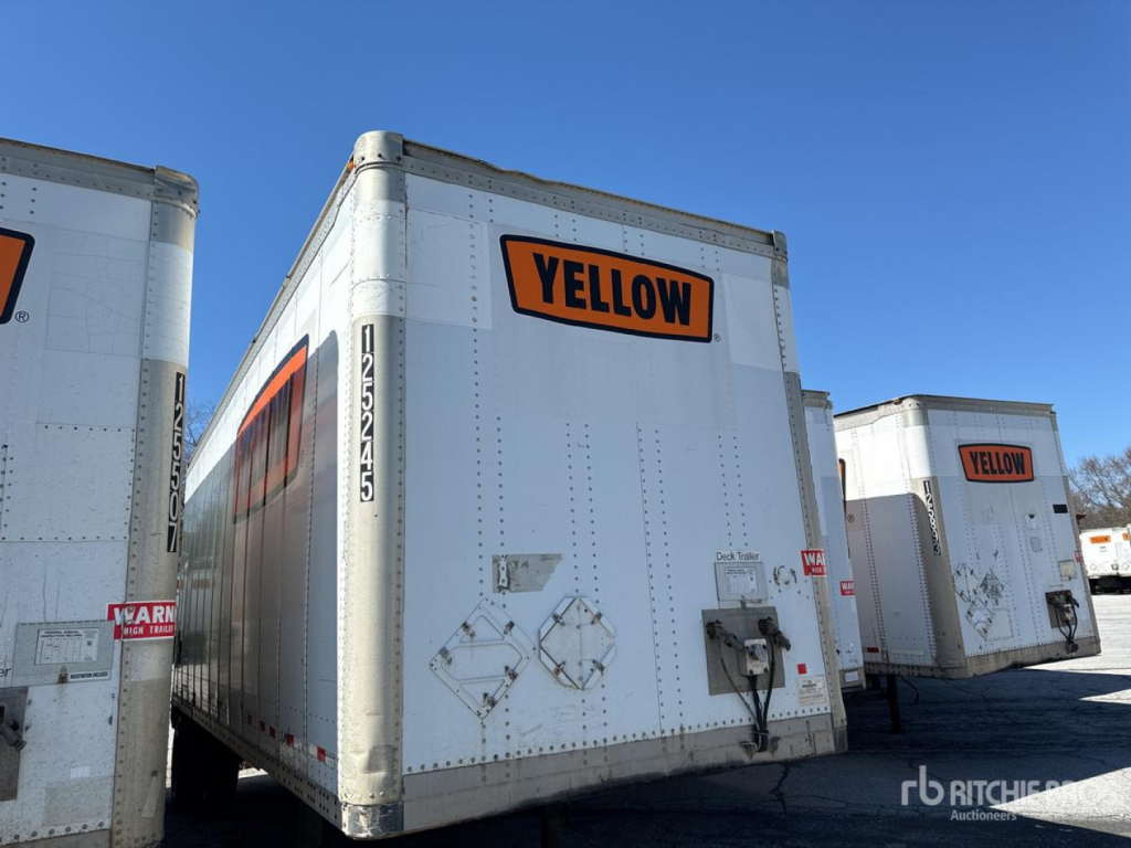 Trailer showing a large white box with a bright yellow YELLOW logo on the back and security latch, side doors, and stacked trailers in a gravel lot.