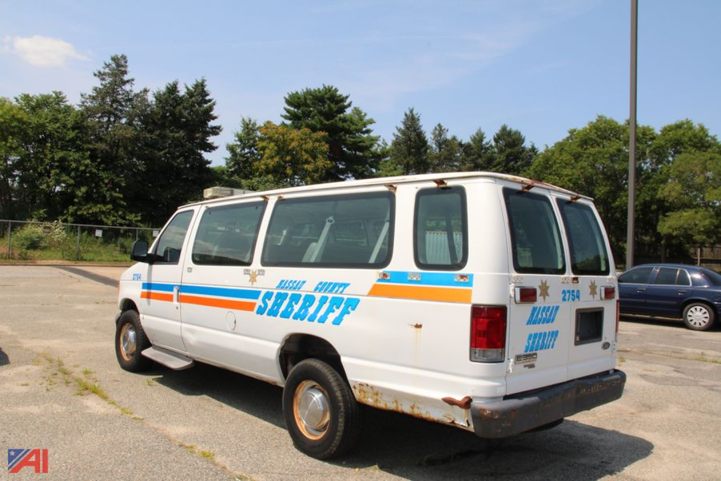 Ford E350 van with sheriff vehicle graphics, rear and passenger side view, white body with blue and orange stripes.