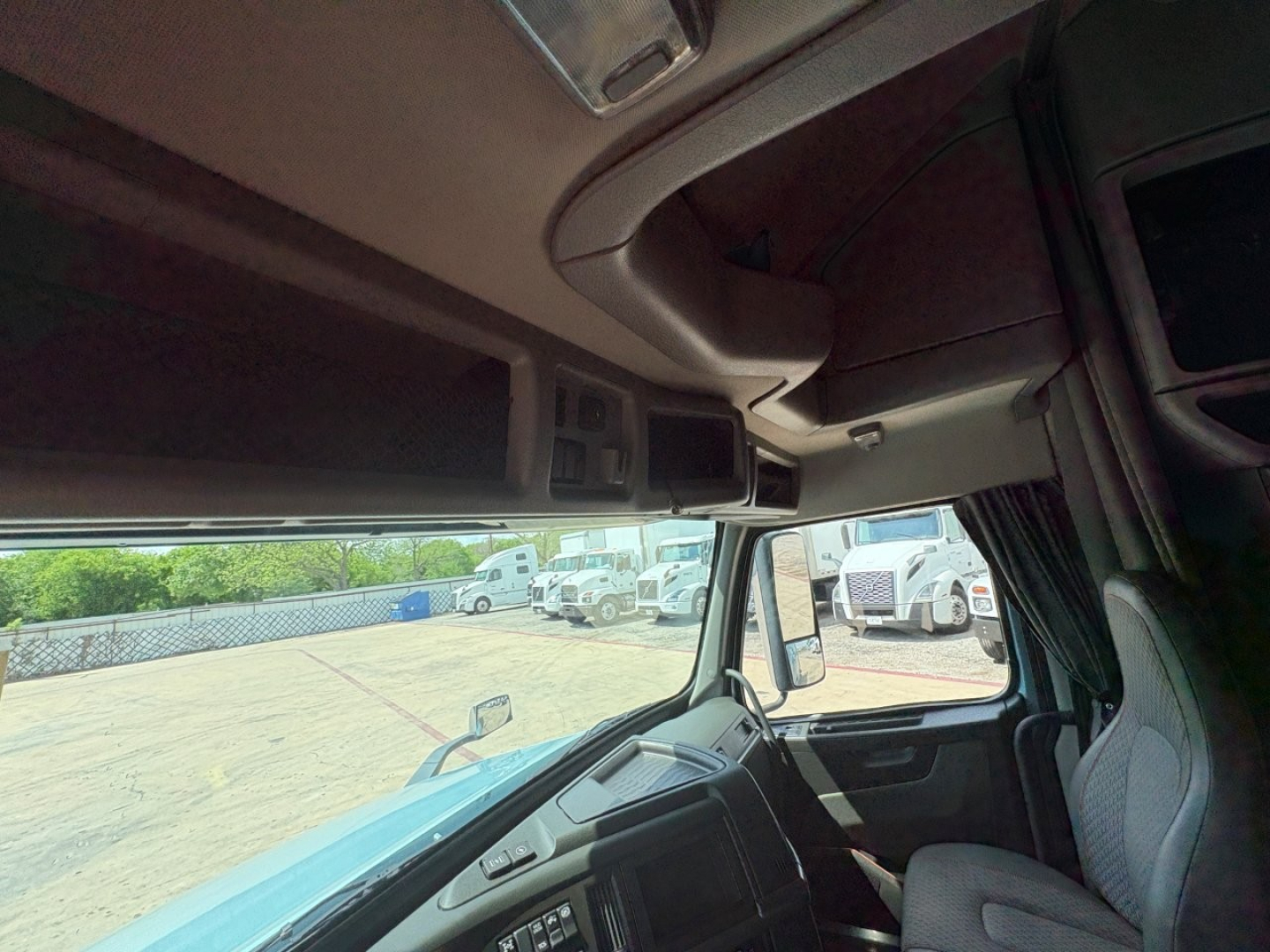 Truck cab interior with overhead storage and steering column visible from passenger side, Volvo VNL cockpit.