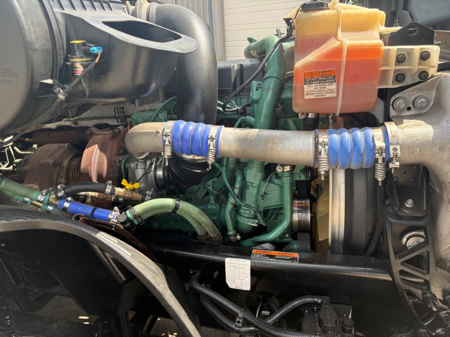 Volvo VNL64T760 engine bay showing coolant reservoir, hoses, belts, and radiator with hoses and clamps.