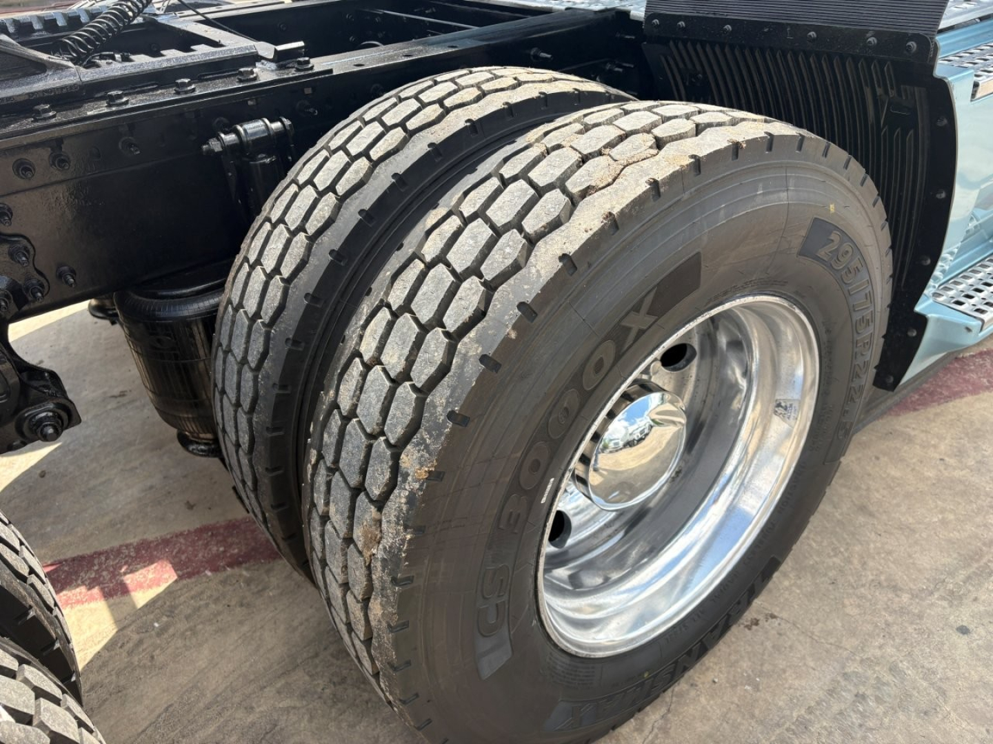 Front wheel and dual rear axle area of a Volvo VNL truck showing Goodyear tire and chrome wheel, chassis frame, and part of the sleeper cab mounting.