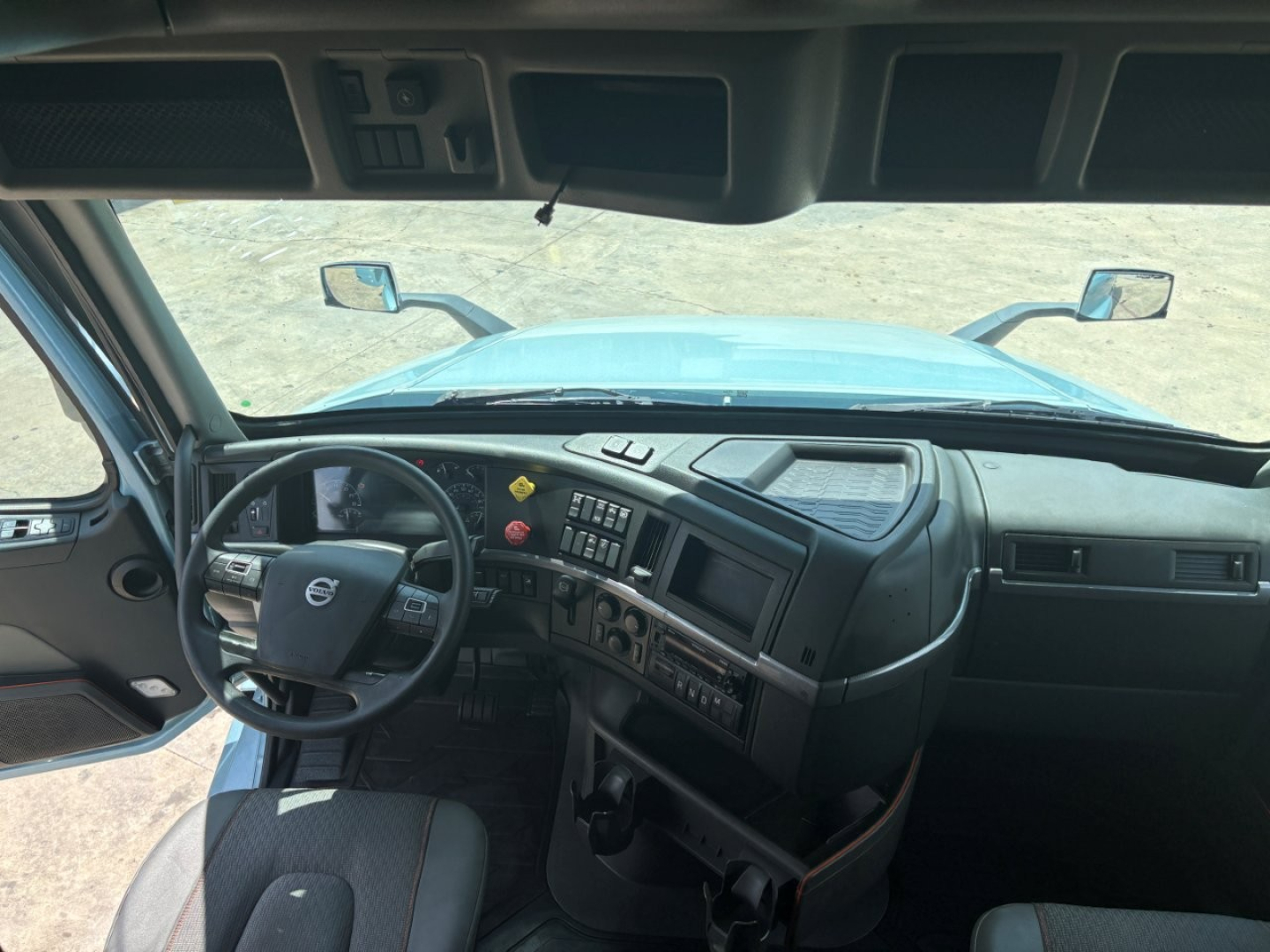 Volvo VNL64T760 interior cab view showing steering wheel with Volvo logo, dashboard controls, radio, and vents.