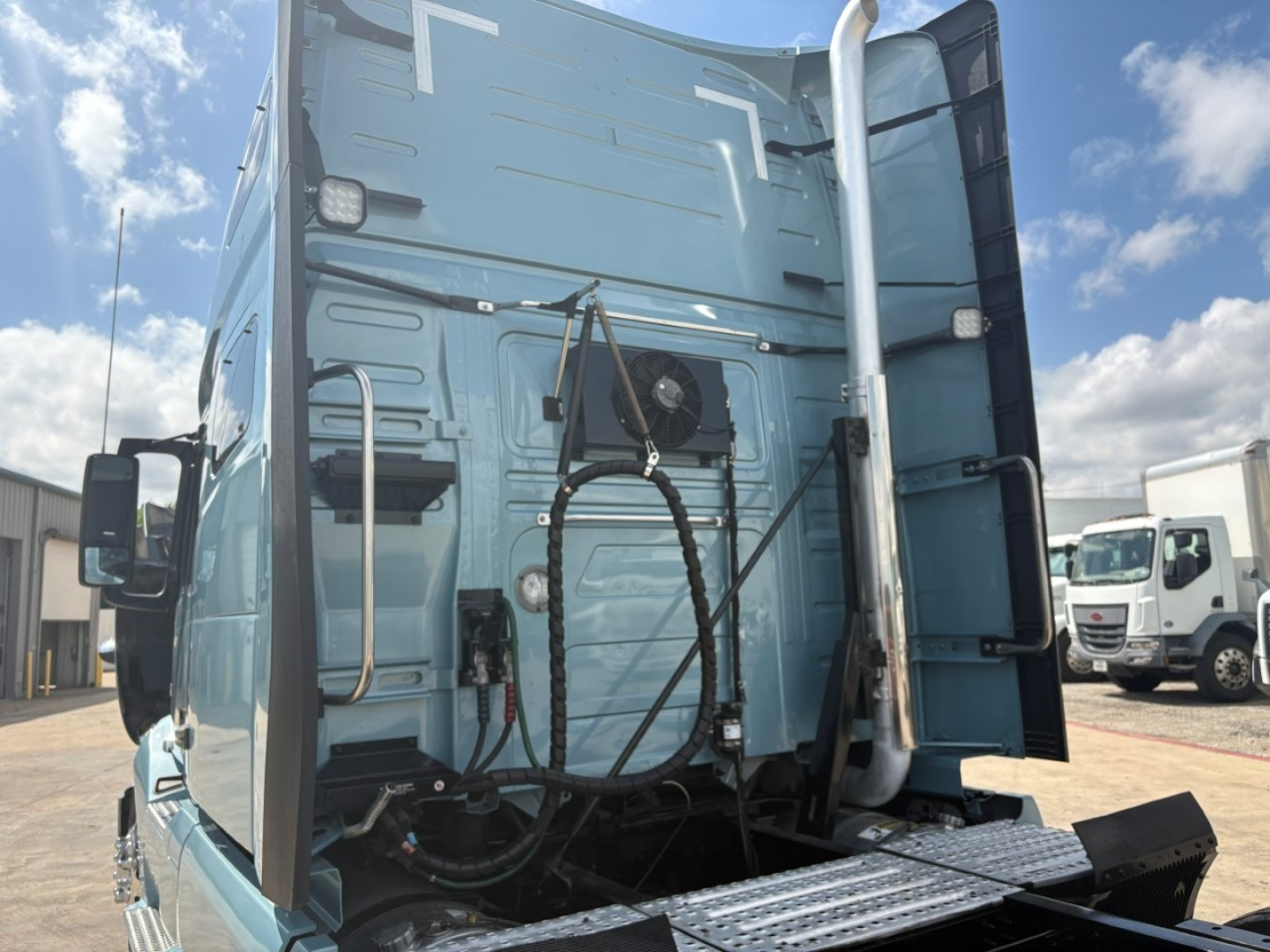 Volvo VNL64T760 truck rear view showing sleeper cab and access ladder with exposed engine compartment area and hoses.