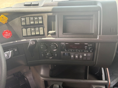 Dashboard of a Volvo truck cab showing various switches, a radio/cassette panel, climate controls, and gear selector. Visible text includes VOLVO on the radio, R N D M gear indicators, and several control labels.