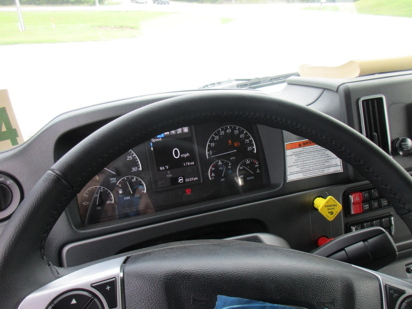 Dashboard view inside a 2027 Freightliner M2 106 truck showing steering wheel, gauge cluster, and warning labels.