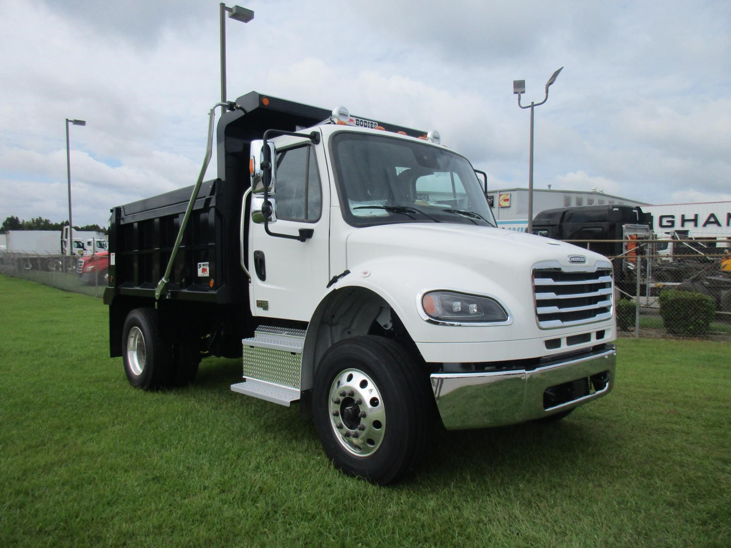 Freightliner M2 106 dump truck in white with black dump bed, front angled view, on grass.
