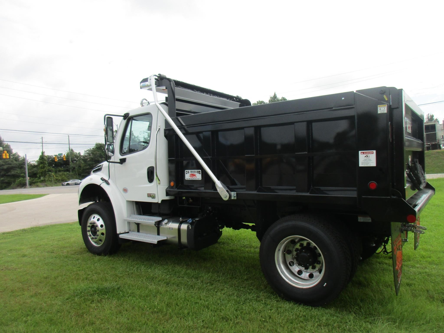 Dump truck body on Freightliner M2 106 with black dump bed and white cab, side view showing steps and front wheel.