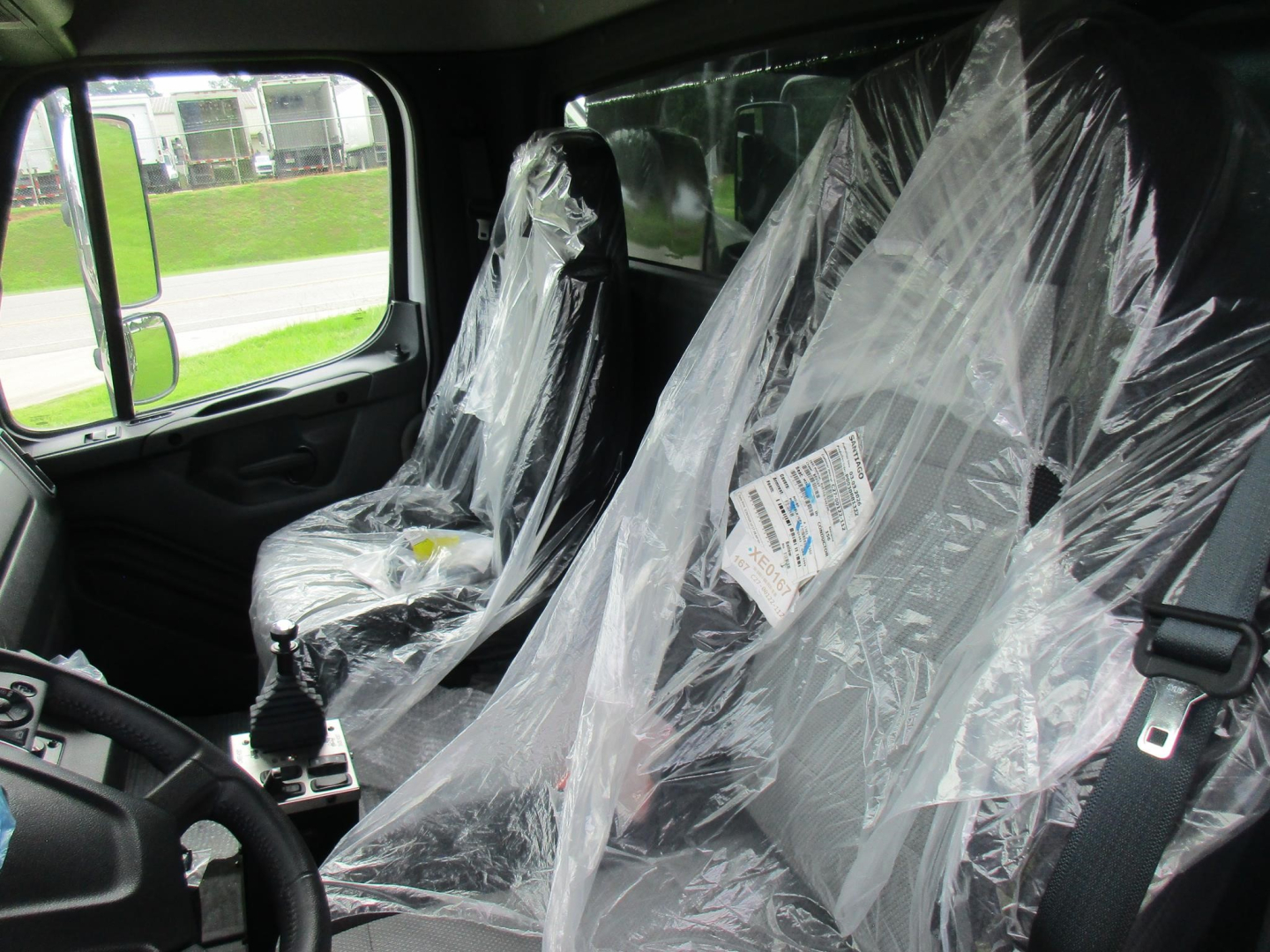 Interior of a Freightliner truck cabin with plastic seat covers, steering wheel visible, label on seat.