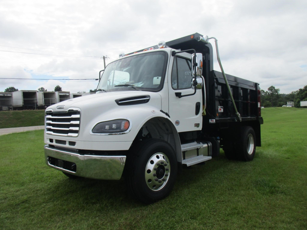 Freightliner M2 106 dump truck in white cab with black dumping bed, front three-quarter view showing chrome grille, headlights, and right-side steps.