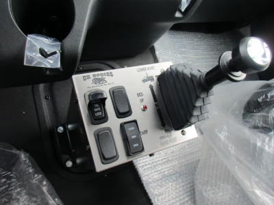 Truck cab interior showing a control panel with switches labeled ON/OFF, and a gear lever with boot; dash area and protective plastic.