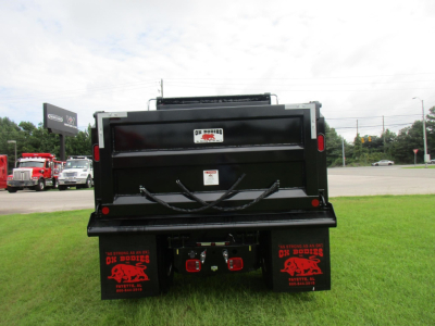 Truck bed of a 2027 Freightliner M2 106 dump truck showing rear view with black dump body and red taillights, mud flaps with graphics, and hitch components.