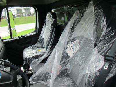 Interior of a Freightliner truck cabin with plastic seat covers, steering wheel visible, label on seat.