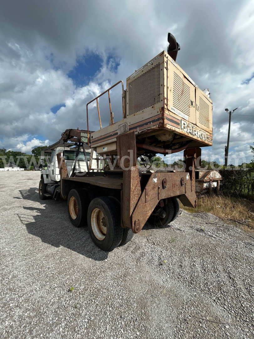 Used 2008 International 74400BA grapple truck on trailer with large rusted metal frame and a beige engine/generator unit mounted on top. Visible text on unit reads 'D-'.
