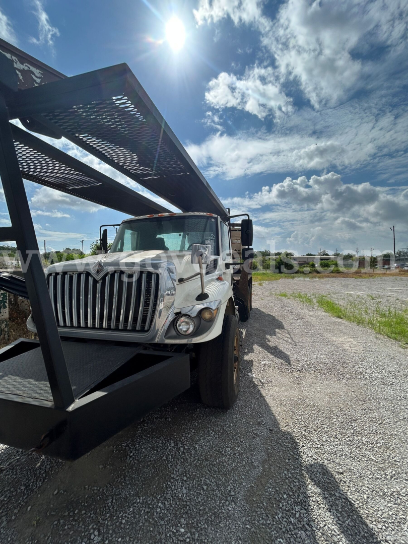 Truck cab and grapple loader on International 7440 series vehicle side view with blue sky background.
