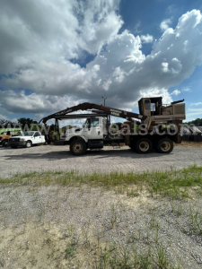 Truck mounted grapple with crane in a gravel lot; International 7440 series cab with long articulated arm over a flatbed; sky with clouds in background.