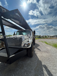 Truck cab and grapple loader on International 7440 series vehicle side view with blue sky background.