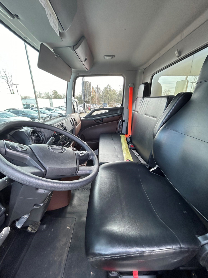Truck cab interior showing steering wheel, driver seat, and bench passenger seat with seat belts visible.