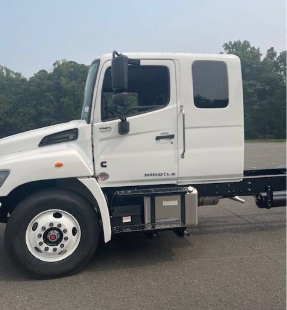 Hino L6 cab chassis truck side view showing white cab and wheel, with side storage compartments and chassis extending rearward.