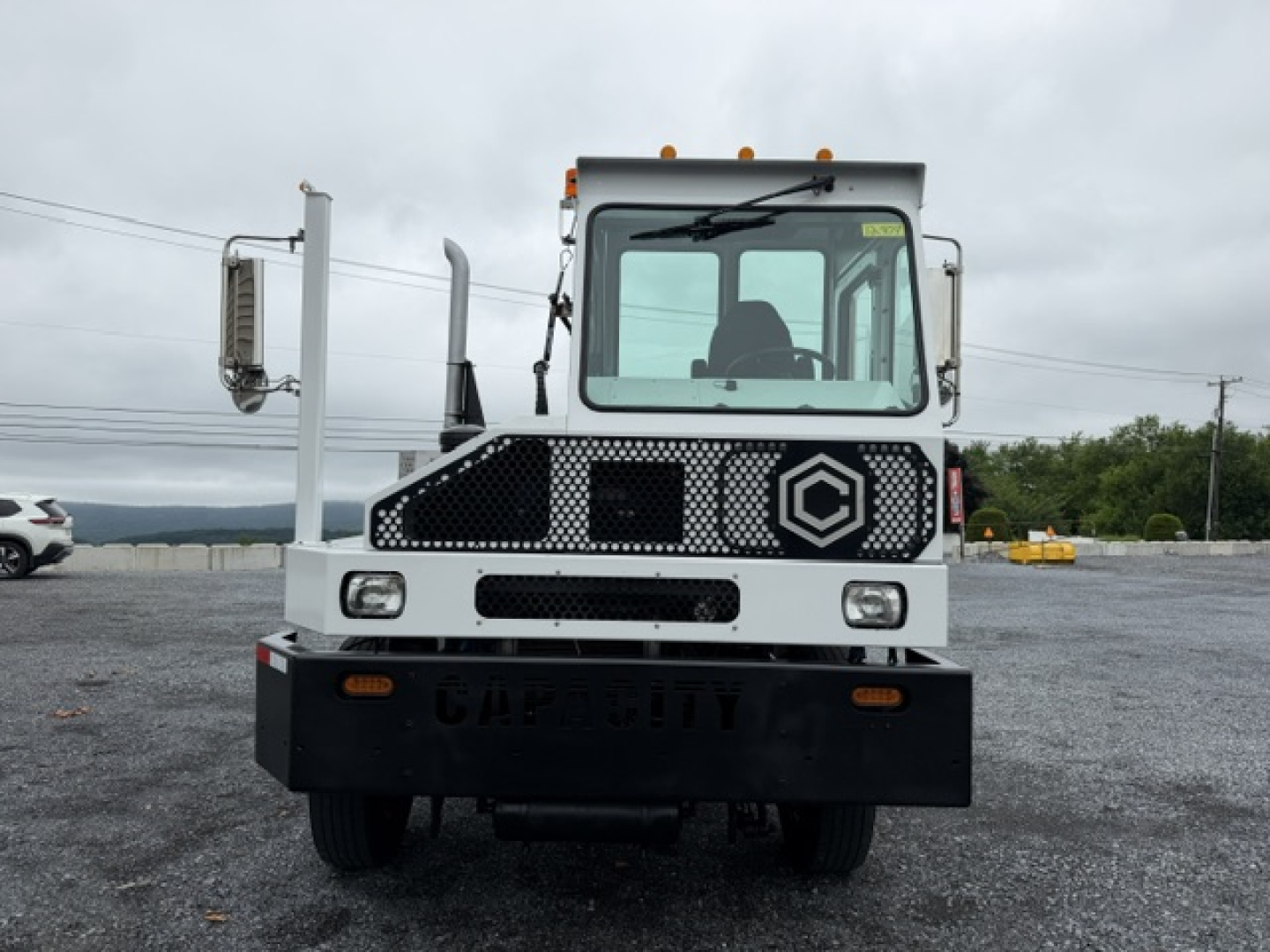 Front view of a capacity TJ6500 yard truck with a white cab, black bumper, and large mirrors. Headlights and grille visible; cab interior seen through windshield.