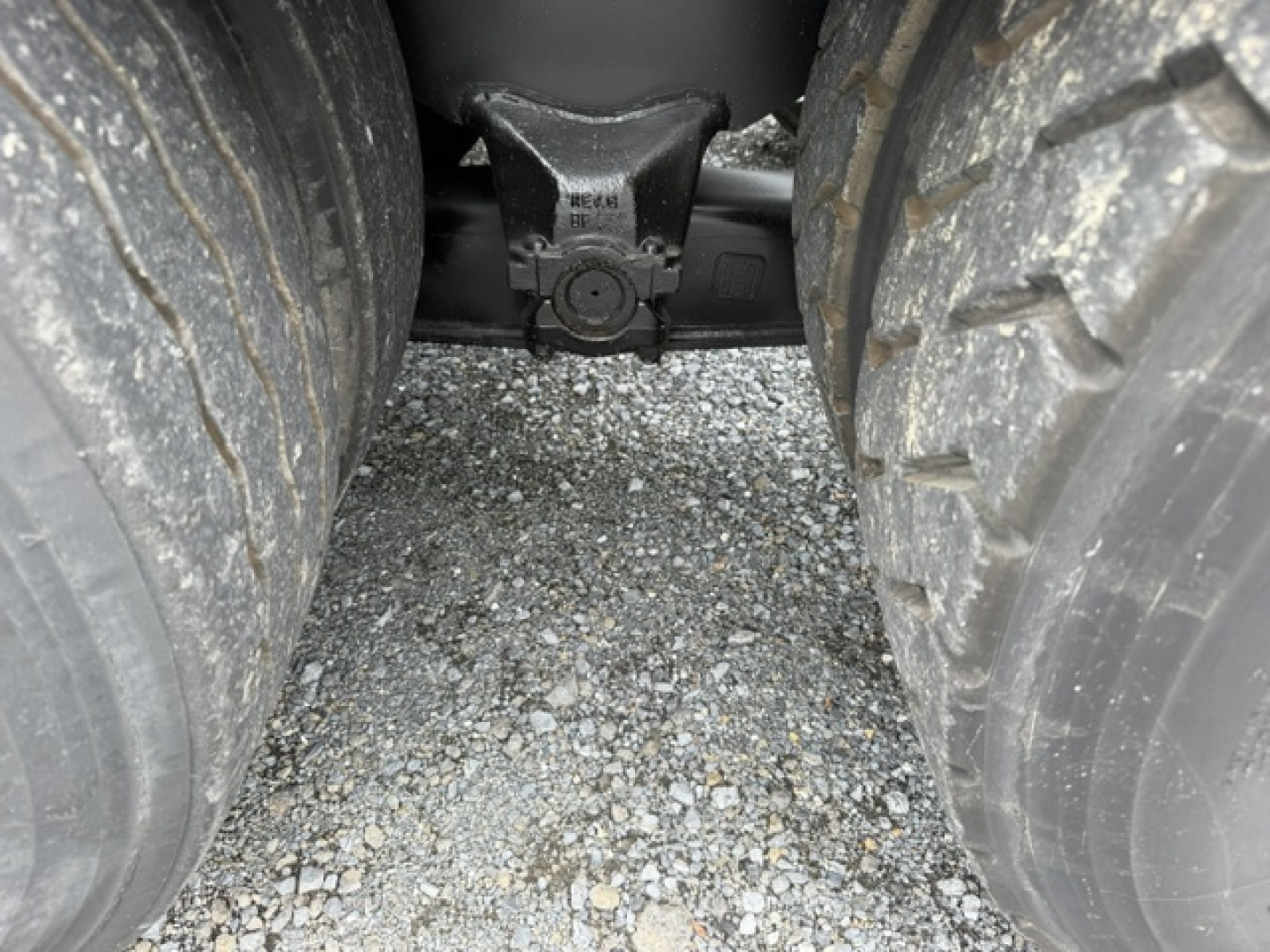 Trailer hitch area between rear dual tires of a Capacity TJ6500 truck showing the hitch receiver and spring assembly.