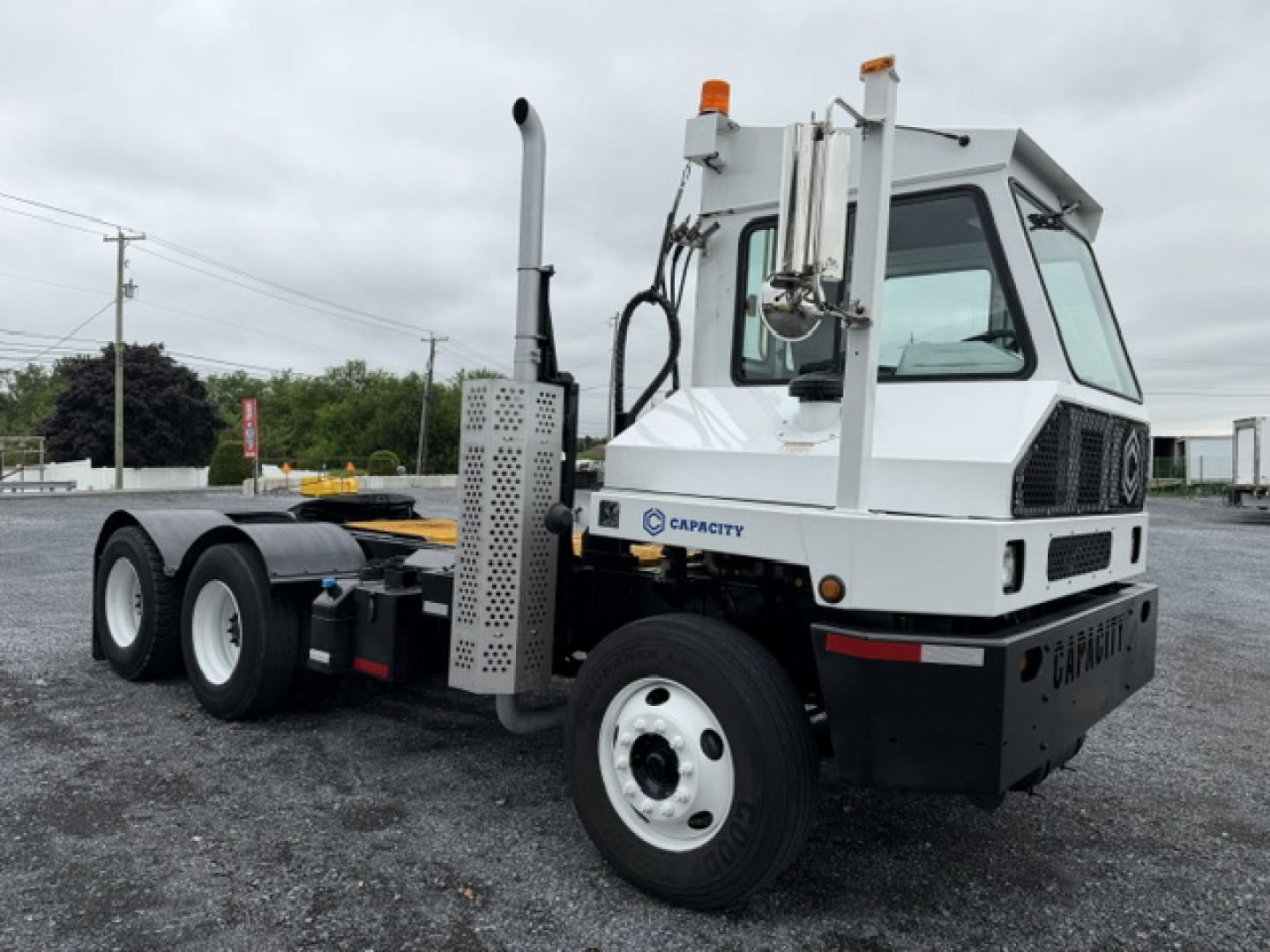 Capacity TJ6500 truck showing side view with cab and chassis, white with black accents, orange beacon lights, exhaust stack, and large wheels.