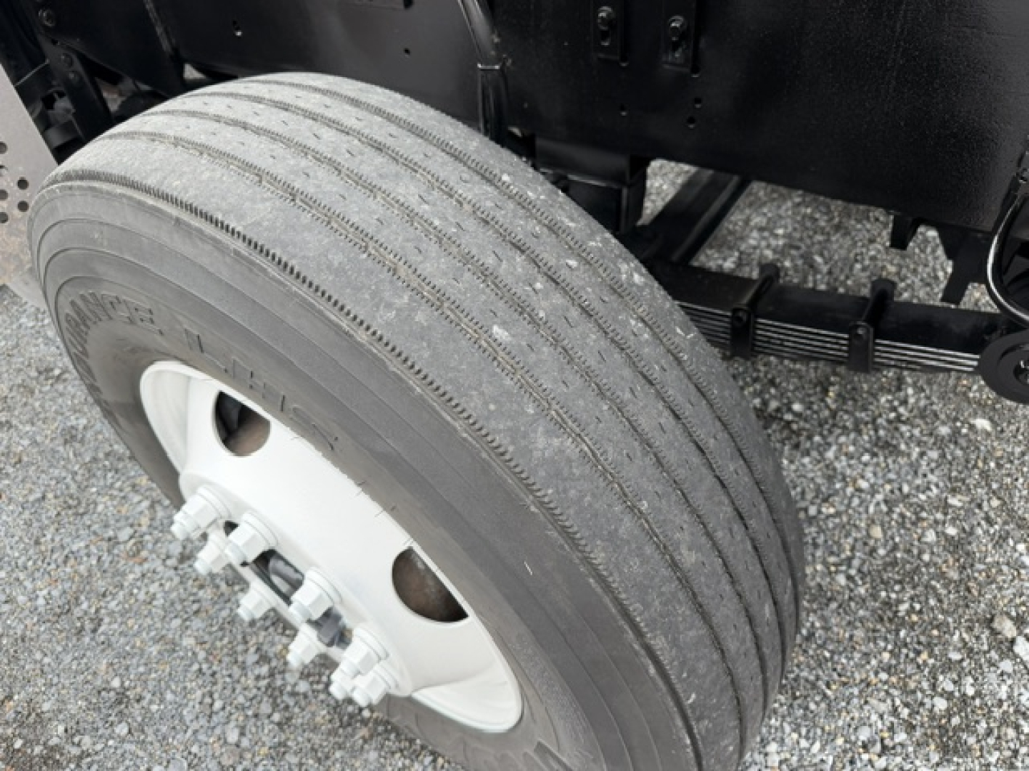 Truck wheel and tire assembly with dual rear axle components and suspension visible; tire tread and wheel hub details; part of chassis underframe visible.