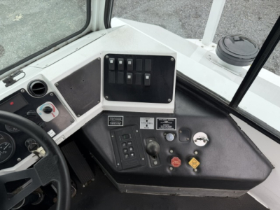 Truck cab dashboard with control switches, gauges, and safety labels; visible are black switch panel, steering wheel, and various warning placards.