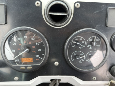 Dashboard of a TJ6500 yard truck showing two round gauges: left speedometer with mph and small digital readout, right tachometer with multiple sub-dials. Center hole above gauges.