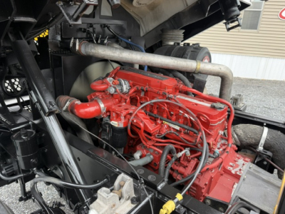 Capacity TJ6500 engine bay showing red diesel engine with hoses, exhaust pipe, and surrounding chassis components.