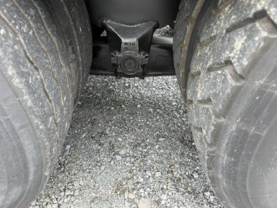 Trailer hitch area between rear dual tires of a Capacity TJ6500 truck showing the hitch receiver and spring assembly.