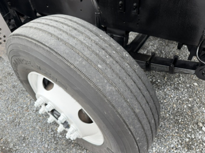 Truck wheel and tire assembly with dual rear axle components and suspension visible; tire tread and wheel hub details; part of chassis underframe visible.