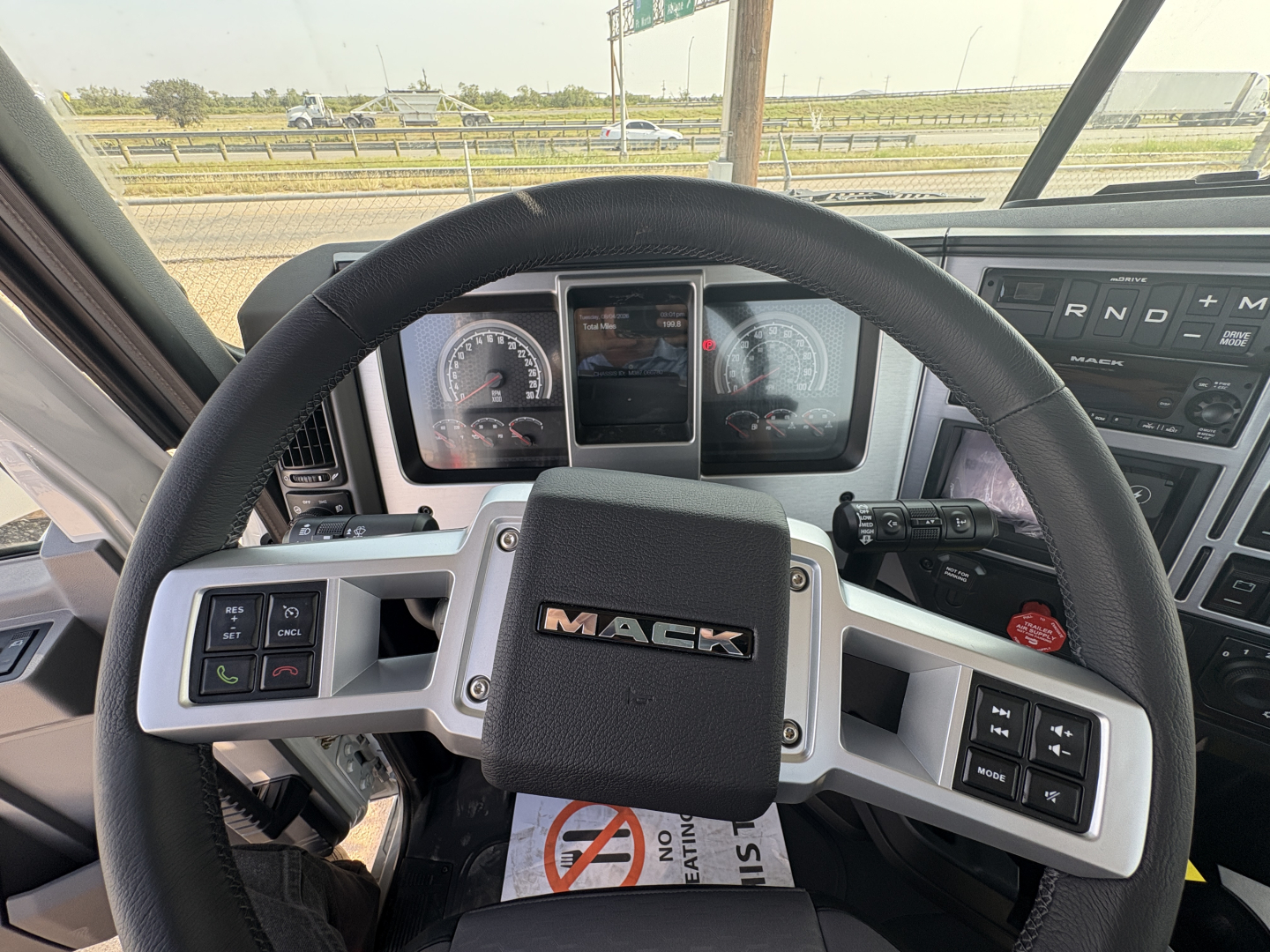 Cab interior of a 2027 Mack GR64FT showing steering wheel with MAC logo and instrument cluster, dashboard controls, and gear selector area.