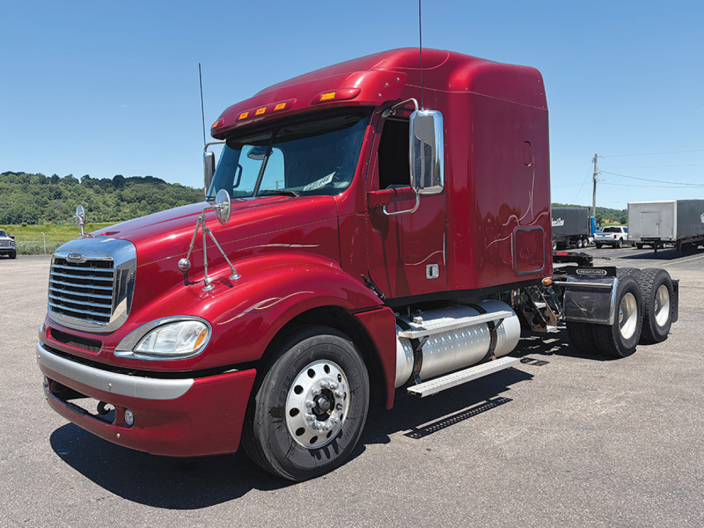 Freightliner CL120 Columbia conventional sleeper truck in red, side view showing chrome fuel tanks and dual rear axles.