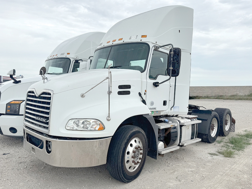 2014 Mack CXU613 conventional daycab truck in a yard, front-left view showing cab, hood, and dual rear axles.