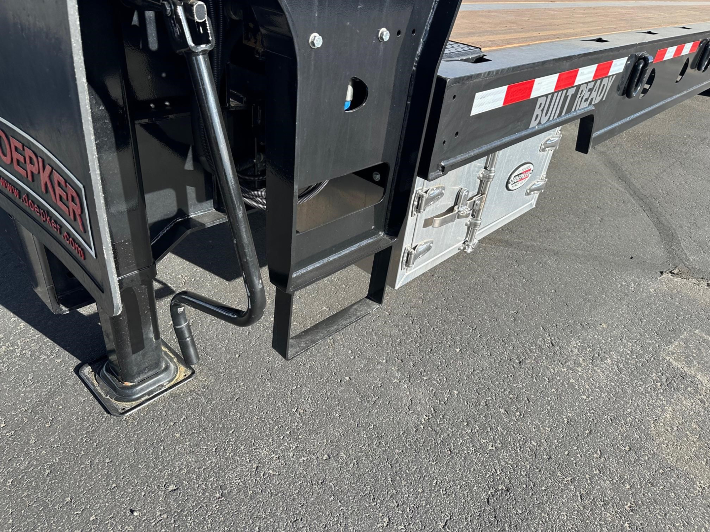 Trailer hitch area of a new 2026 Doepker RT trailer showing landing gear leg, frame, and storage box with Doepker branding.