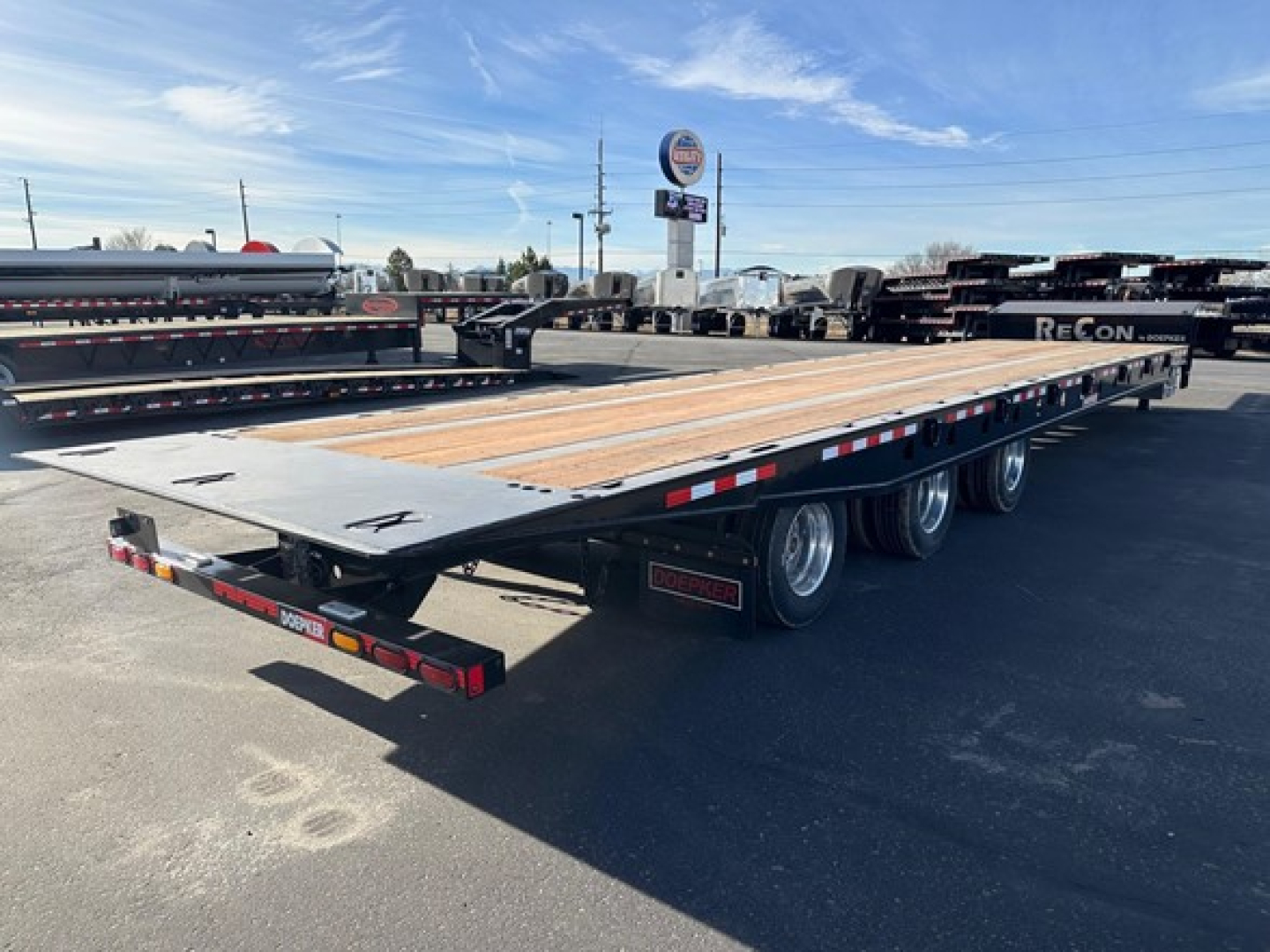 Doepker tridem trailer showing flatbed deck with multiple axles and wooden decking, side rails and rear lights.