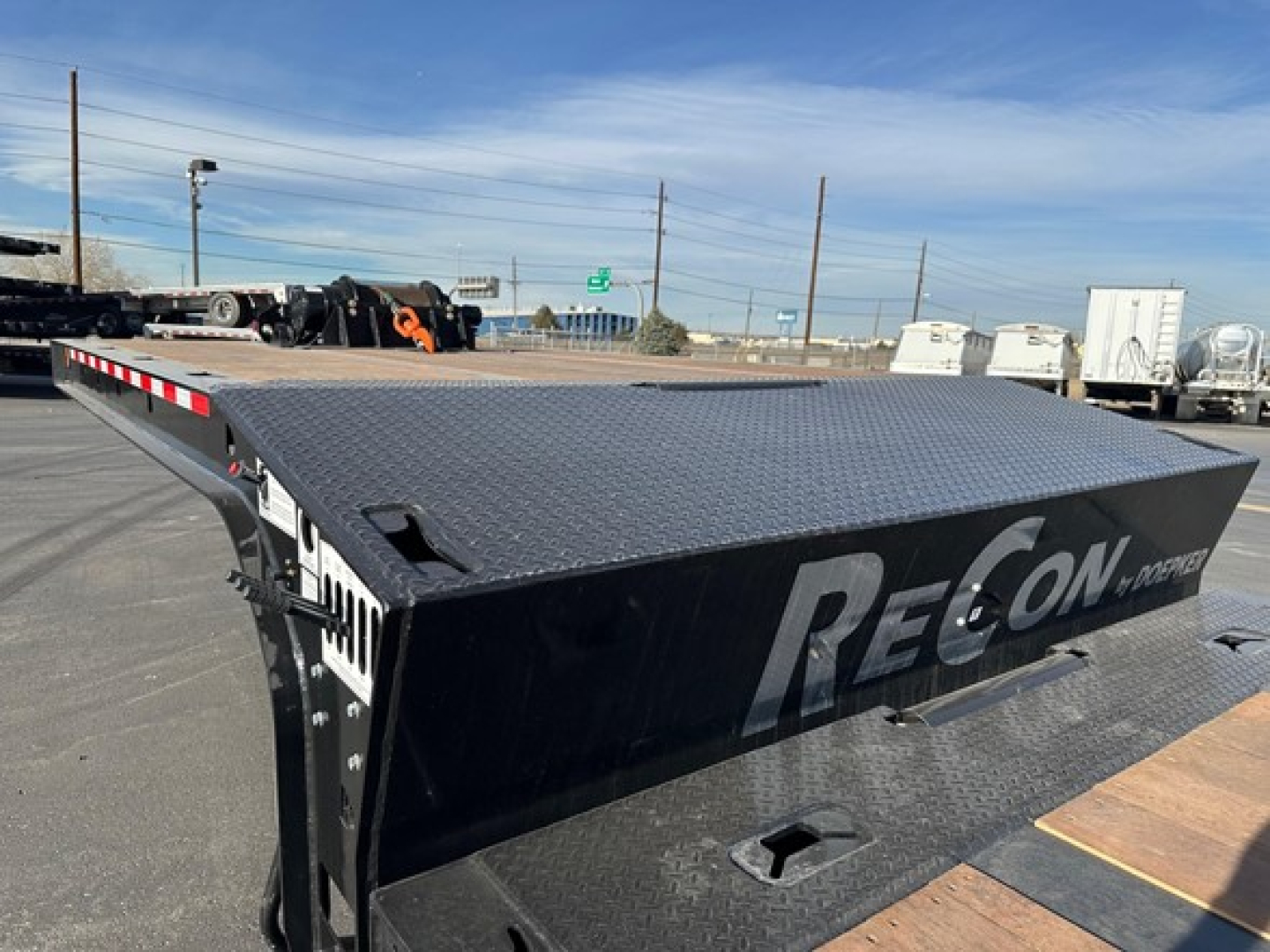2026 Doepker Tridem Rt trailer with a diamond plate deck and RECON or RECON branding on the side; logo and partial text visible on black steel frame.