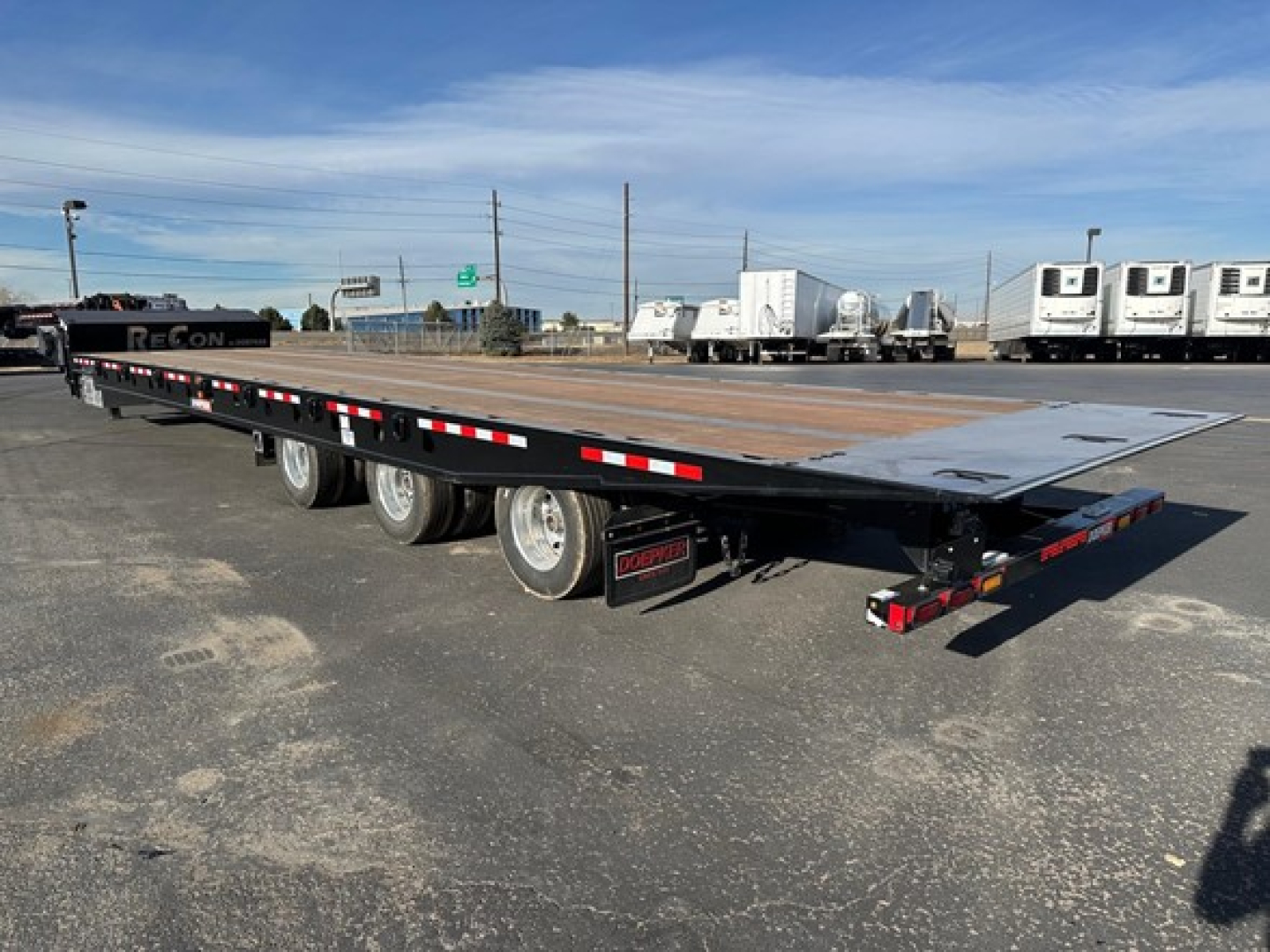 Doepker tridem RT trailer flatbed side view showing long deck, triple axle, and rear ramps.