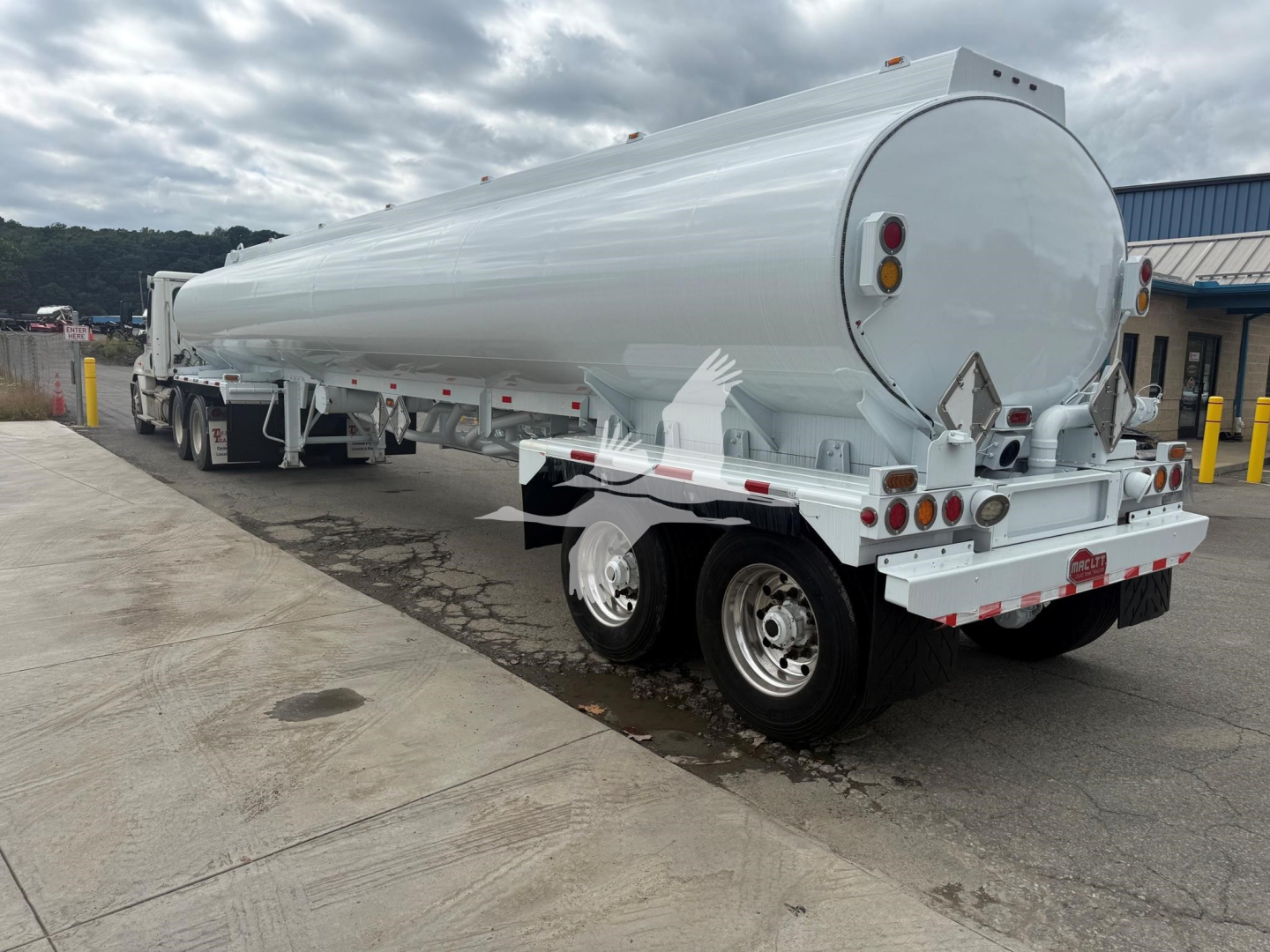 Tank trailer showing cylindrical tank with rounded rear end and dual rear axles, white exterior, rear lights, and support frame.