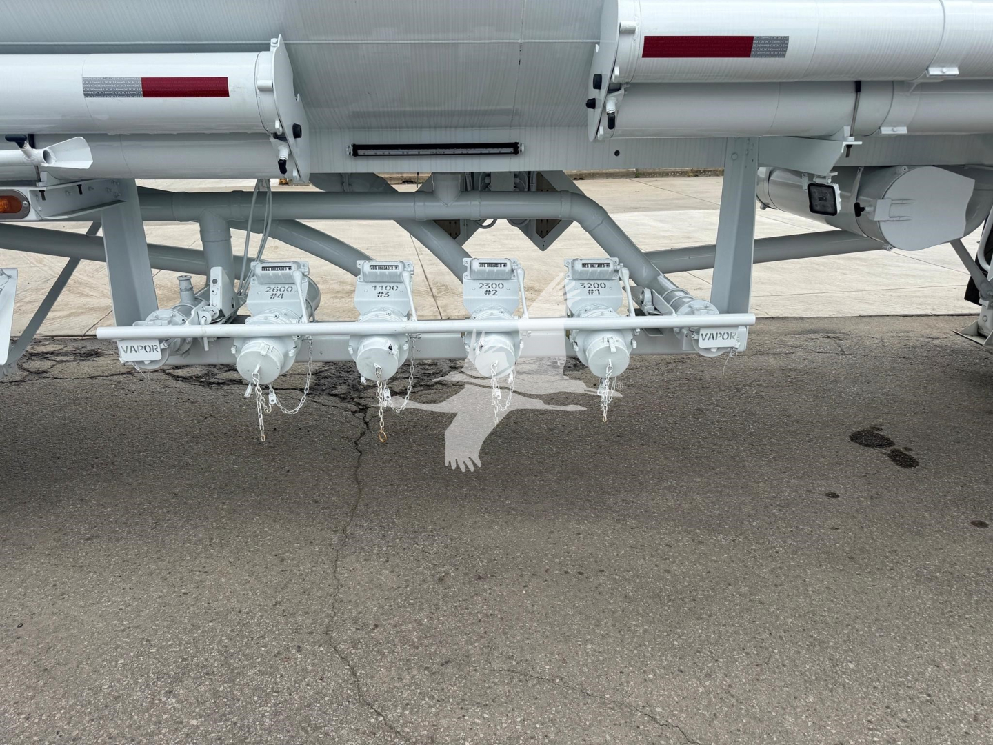 Trailer undercarriage showing multiple white valves and piping for fuel transfer on mac petro tank trailer with VIN tag and stock number visible.