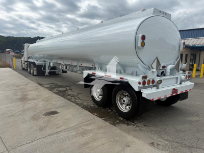 Tank trailer showing cylindrical tank with rounded rear end and dual rear axles, white exterior, rear lights, and support frame.