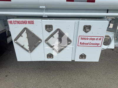 White fuel trailer side compartments with diamond-shaped access panels and warning labels. Text reads: 'FIRE EXTINGUISHER INSIDE' upper left panel; 'Vehicle stops at all Railroad Crossings' on right panel; additional small labels and latche