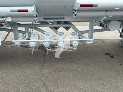 Trailer undercarriage showing multiple white valves and piping for fuel transfer on mac petro tank trailer with VIN tag and stock number visible.