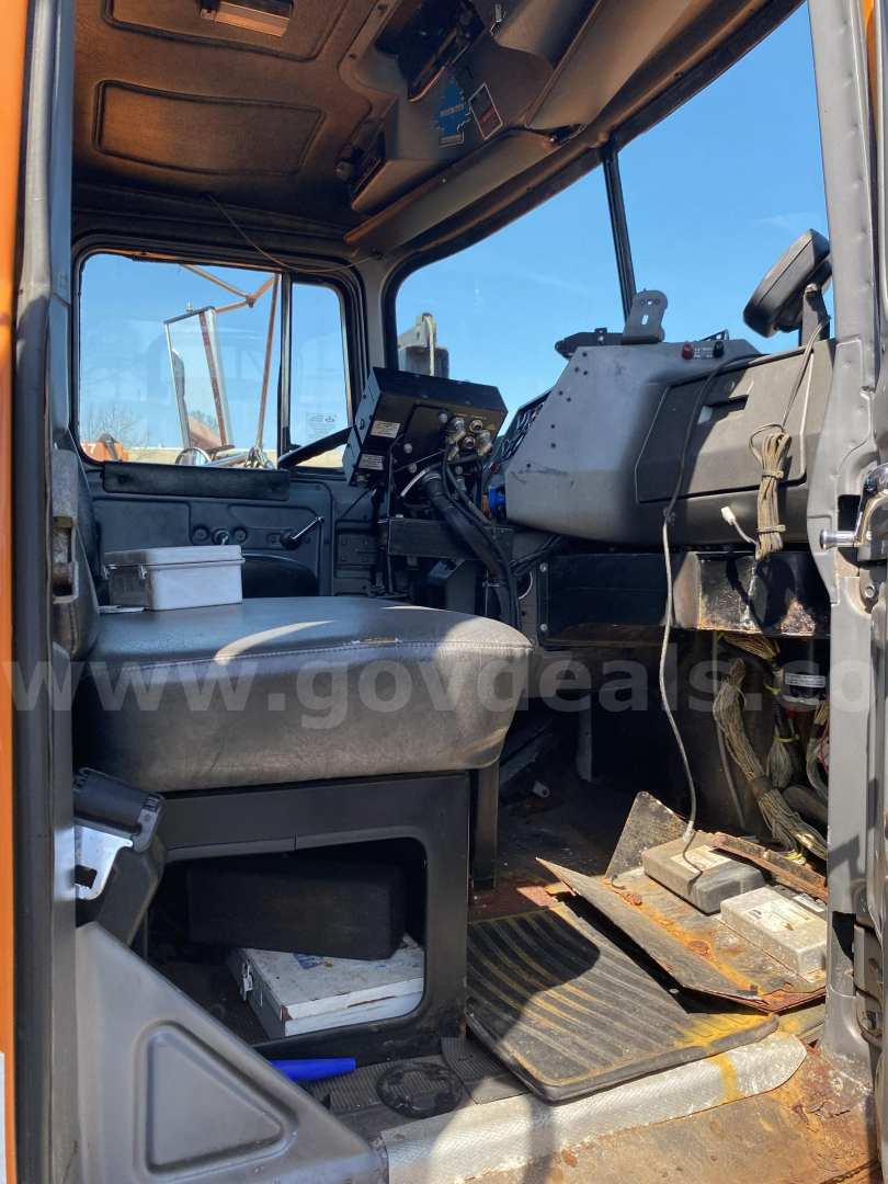 Cab interior of a 2004 Mack RD688P plow truck showing driver seat, dashboard, steering wheel, and pedals.