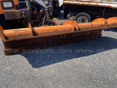 Mack RD688P plow attachment in front of trucks showing orange metal blade with wear and hydraulic components.