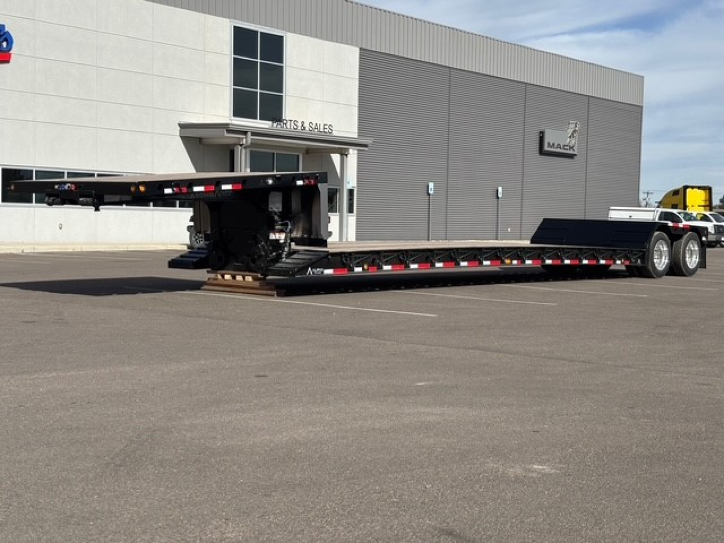 Alpha A80MG lowboy trailer with double drop and swingouts, black with red/white safety markings, parked outside a dealership.