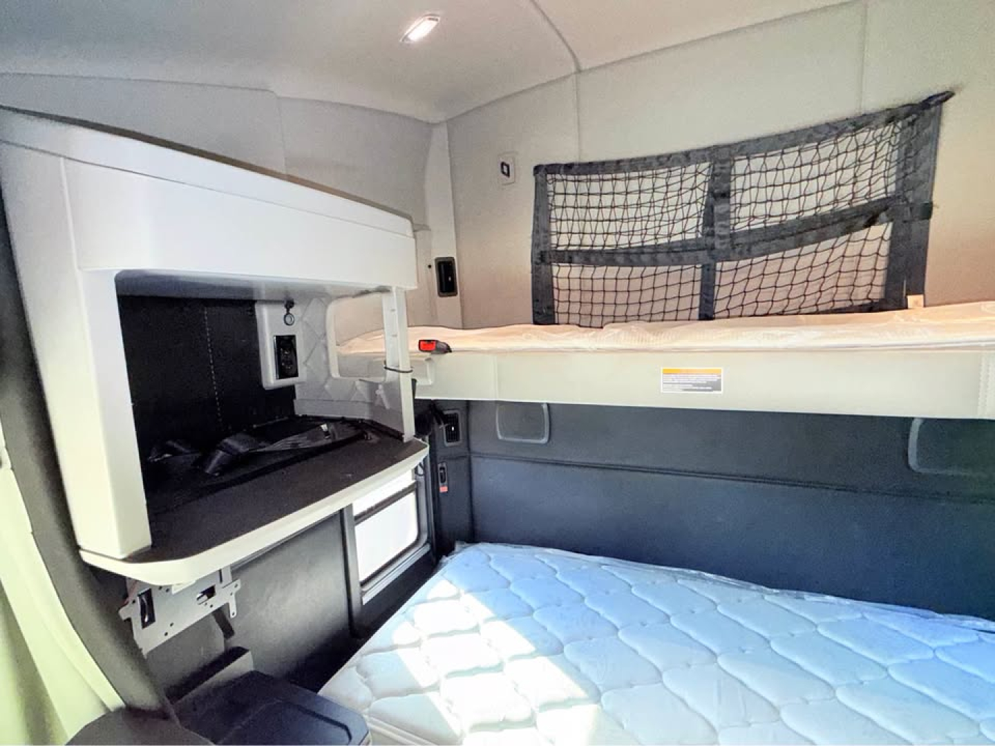 Kenworth T680 interior sleeper cab with bunk bed area and overhead storage; visible are side shelf, small fridge, and a window netting.