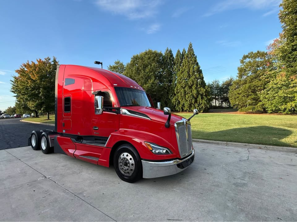 Kenworth T680 tractor in red, front and side view, with chrome bumper and mirrors, clear sky, trees in background.